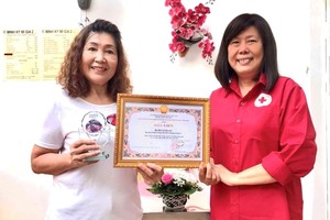 第六郡红十字会主席黎氏宝庄向何丽娟（左）颁奖。