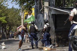 当地时间2023年3月3日，海地首都太子港总统府附近，一名男子抱着孩子经过海地国家警察，试图击退黑帮。（图：AFP）