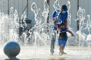 2020年8月13日，在科威特首都科威特城，一名父亲带着孩子在高温天气下的喷泉里玩耍。（图：新华社）