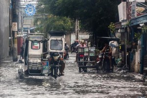 7月26日，人们在菲律宾马拉邦一处积水的街道涉水而行。（图：新华社）