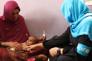 在阿富汗首都喀布尔，一名卫生工作者上门为一名营养不良的小孩看诊。（图：UNICEF）