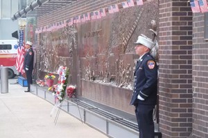 世贸中心遗址旁的消防员纪念墙上插满国旗并摆放了花圈，以纪念在22年前牺牲的343名消防员。（图：互联网）