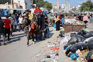 2023年10月16日，在加沙地带南部的汗尤尼斯，巴勒斯坦人从成堆的垃圾旁经过，这些垃圾有可能引发一场环境灾难。 （图：路透社）