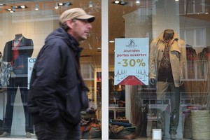 一名男子从比利时布鲁塞尔一家贴有打折资讯的店铺前走过。（图：新华社）