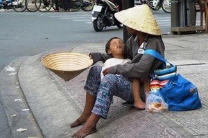 一名乞丐抱着小孩坐在路旁行乞。（示意图：越通社）