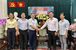 第五郡委委员、人委会副主席阮武春奇（左三）向本报编委文忠孝赠送鲜花祝贺。