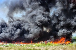 图为3月13日上午，平新郡一块数十公顷空地上的垃圾场冒出滚滚浓烟，火势迅猛，威胁到周围的停车场。（图：孟玲）