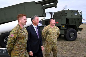 澳洲国防部长马尔斯（中）3月24日出席澳洲国际航展，他与两名士兵在一辆高机动炮兵火箭系统（HIMARS）旁拍照。（图：AFP）