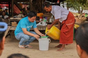 在灾情严重的曼德勒，儿基会工作人员正与当地村民向社区民众示范净水片的使用方法。（图：联合国）