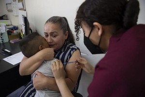 一名妈妈怜惜地抱着四岁儿子，让他接受麻疹疫苗接种。（图：AP）