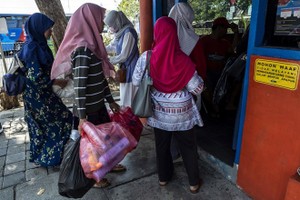 Dozens of people clutching bags full of plastic bottles and disposable cups queue at a busy bus terminal in the Indonesian city of Surabaya. (Photo: AFP)