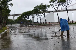 Lực lượng chức năng cào dọn lớp đất, cát bị sóng đánh tràn vào. Ảnh: XUÂN QUỲNH