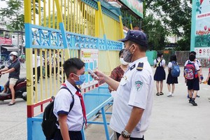 School security guard takes temperature of a student before he enters the school. (Photo: SGGP)