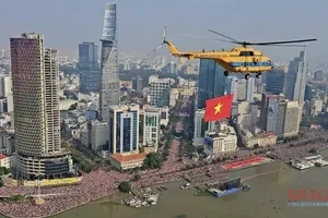 A helicopter carrying the national flag soars across the sky over Ho Chi Minh City (Photo: SGGP)