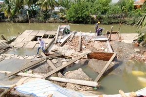 Tranh thủ thủy triều xuống, thực hiện tháo dỡ căn nhà bị sạt lở, khơi thông dòng chảy. Ảnh: LONG HẬU