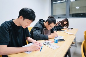 学生用造型压笔在银色锡纸上勾勒秦汉器物纹样。