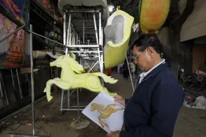 Nghệ nhân Văn Tòng kiểm tra và so sánh giữa thiết kế kỹ thuật bản vẽ và mô hình đang thi công. Ảnh: DŨNG PHƯƠNG