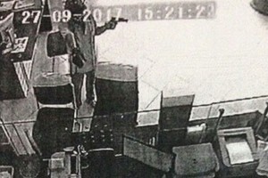 根據該銀行監控提取的圖片，歹徒蒙面戴著安全帽，左手持著狀似手槍，右手拿著手提袋扔進交易櫃台，強迫人員把錢放進手提袋。（圖源：明英）