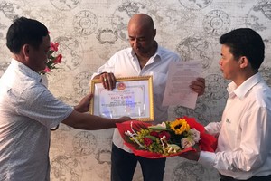 峴港市蓮沼郡郡委書記武功政(右一）和該郡人委會副主席阮友鐵(左一)向法籍遊客讓‧克里斯托夫頒贈獎狀並送鮮花。（圖源：阮秀）