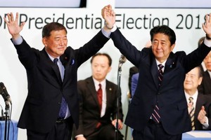 日本首相安倍晉三（右）在東京自民黨總部再次當選該黨領袖後與前國防部長石破茂舉起雙手。 （圖源：路透社）