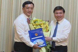 新任市人委會辦公廳主任何福勝（左）從市人委會主席阮成鋒手中接過人事委任《決定》和祝賀鮮花。（圖源：明蓉）