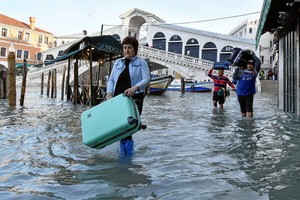 當地時間12月23日，意大利威尼斯的里亞托橋附近，一名女性拎著箱子涉水而行。 （圖源：路透社）