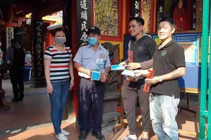 溫陵會館理事吳麗株(左一)與保安員向沒有戴口罩的善信派發口罩。