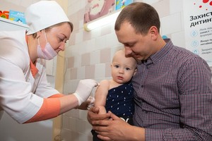 一名嬰兒被父親抱在懷中，接受護士接種的第一劑麻疹、腮腺炎和風疹三聯疫苗。（圖源：Unicef）