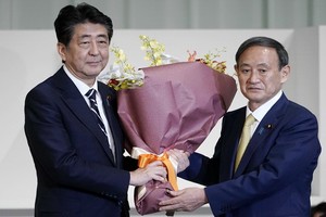 日本內閣官房長官菅義偉（右）當選自民黨新總裁後向安倍晉三獻花。（圖源：AFP）