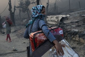 9月9日，希臘萊斯博斯島的莫里亞難民營發生大火後，一位移民帶著自己的物品離開難民營。（圖源：路透社）