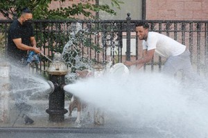 當地時間2020年7月27日，兩名青年在紐約布魯克林街道上噴水的消防栓前嬉水消暑。（圖源：Getty Images）