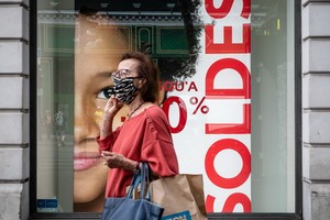 7月15日，一名女子戴口罩走過法國巴黎街頭一處打折季的廣告牌。（圖源：新華社）