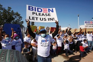 來自中美洲和其他民族的移民在美墨邊境附近聚集並高舉標語，籲拜登讓他們進入美國。（圖源：路透社）