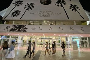 人們走過法國嘎納電影宮外的電影節海報。（圖源：互聯網）