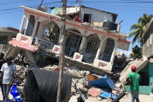 8月15日，在海地萊凱，人們站在一棟被地震損毀的房屋前。（圖源：新華社）