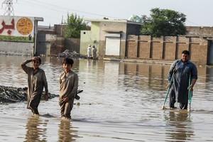 在巴基斯坦开伯尔-普赫图赫瓦省受灾最严重的地区之一瑙谢拉卡兰，两个男孩和一名拄着拐杖的男子穿过被洪水淹没的街道。（图：联合国）
