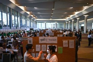 5月7日，在5月14日大选前一周，一名选民（前右）在曼谷一家购物中心内的投票站提前投票，询问投票方向。（图：AFP）