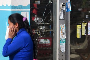 图为2023年1月19日，在秘鲁安第斯山脉城市库斯科，警察击退了占领机场场地的抗议者，一名妇女在一块被弹丸击碎的玻璃旁讲电话。（图：Getty Images）