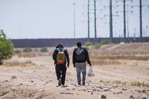 两名男子走在分隔墨西哥和美国的边境墙旁边。（图：国际移民组织）