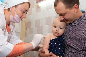 一名婴儿被父亲抱在怀中，接受护士接种的第一剂麻疹、腮腺炎和风疹三联疫苗。（图：儿基金）