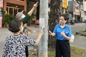 市民与职能力量协力清除路灯柱上的违规广告产。（图：志石）