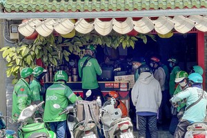 在胡志明市庆会坊孙诞街一家商店，网约车司机等候领取顾客通过应用程式订购的餐食。图：黄雄