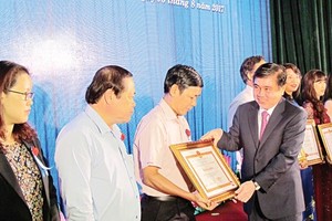 Chairman of the HCMC People’s Committee Nguyen Thanh Phong gives certificates of merit to individuals and organizations well performing tax obligations on August 3 (Photo: SGGP)