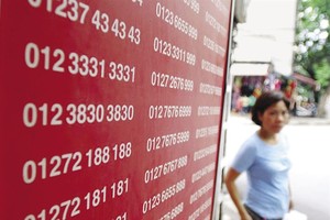 A woman walks past a board showing telephone numbers on sale. (Photo: laodong.vn)
