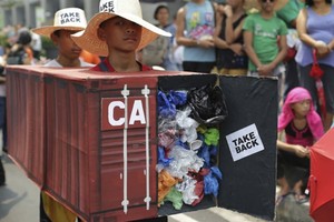 Filipino environmental activists wear a mock container vans filled with garbage to symbolize the 50 containers of waste that were shipped from Canada to the Philippines two years ago as they hold a protest outside the Canadian Embassy in the financial dis