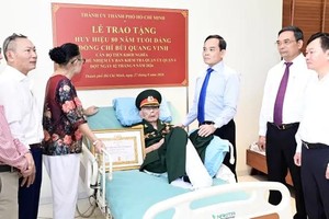胡志明市市委书记陈留光向裴光荣同志颁授80年党龄纪念章及问候同志的健康状况。图：文明