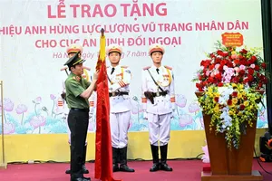 Bộ trưởng Lương Tam Quang trân trọng gắn danh hiệu Anh hùng lực lượng vũ trang nhân dân lên lá cờ truyền thống của Cục An ninh đối ngoại. Ảnh: Cổng thông tin Bộ Công an