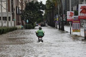 一名送货员骑车经过泰国暖武里府蒙通他尼地区一条积水道路。图片来源：BANGKOK POST