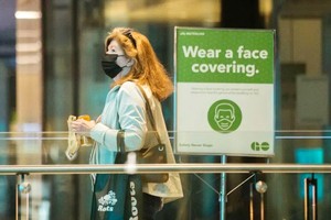 在加拿大多倫多一座車站，一名戴口罩的女子從提醒人們戴口罩的告示旁走過。