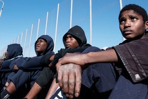 坐在利比亞拘留中心院子裏的移民。